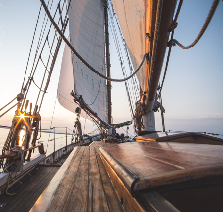 The deck of a boat with sails and the ocean in the background